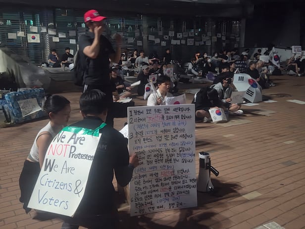 6일 오후 11시쯤 서울 송파구 잠실 투표소 앞. 집회 안내문 뒤로 야간 집회에 참여하는 시민들이 앉아 구호를 외치고 있다./김도연 기자